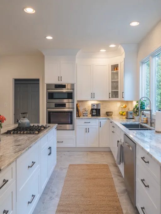 Bright white kitchen with a marble topped island and a run of wall ovens